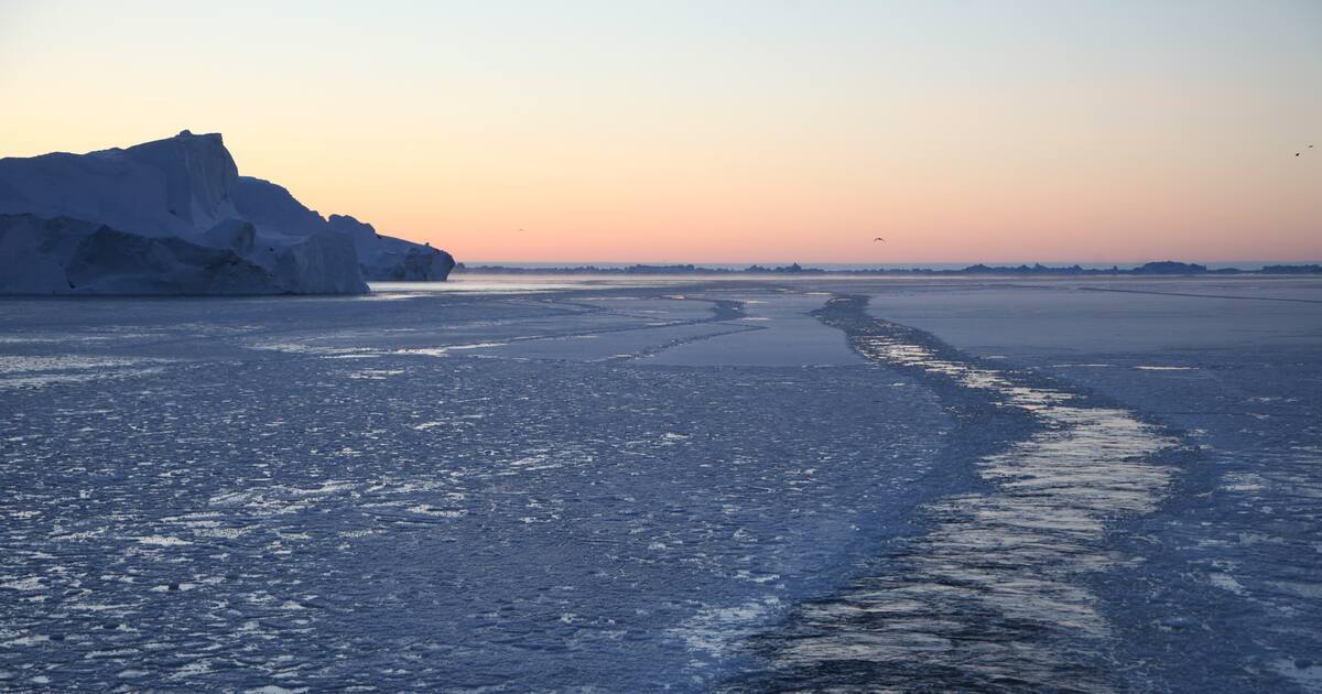 Ein Eisbrecher hat sich den Weg durch den teils zugefrorenen Ilulissat-Eisfjord gebahnt, während daneben riesige Eisberge in die Höhe ragen.