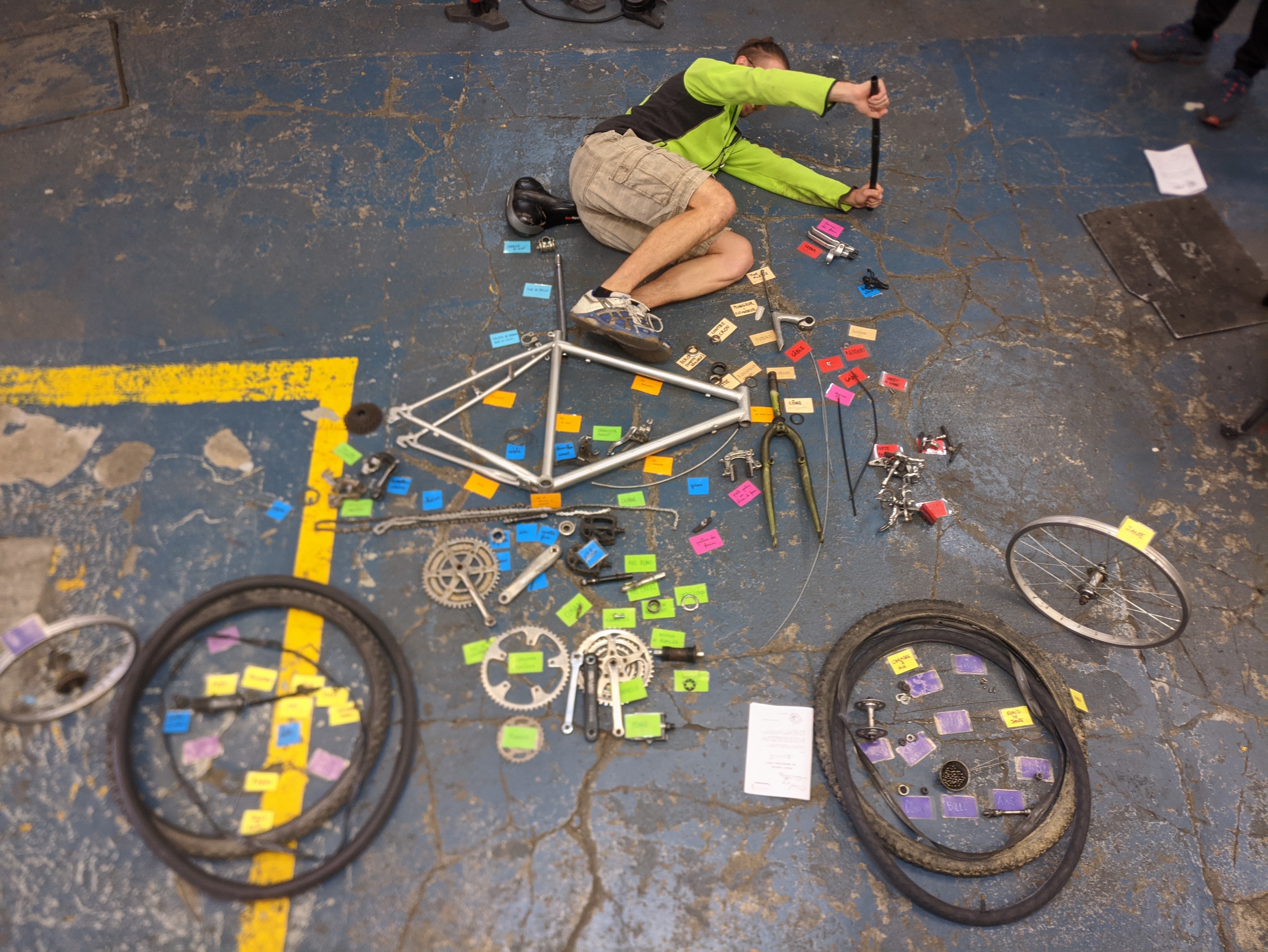 Éclaté de vélo au sol avec pièces de vélos et étiquettes. Une personne est couchée sur le côté, faisant semblant de rouler.