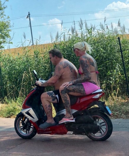 Twee half ontklede zwaar getatoeëerde mensen op een scooter