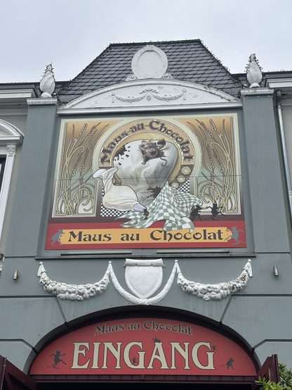 An art nouveau styles illustrated sign that says ‘Maus au Chocolate’ with a cute little mouse next to a baker’s icing bag.