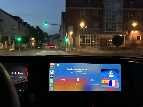 Blick aus dem Inneren eines Autos in der Nacht, sichtbares Armaturenbrett mit einem Bildschirm mit einer Live-Übertragung für ein Spiel zwischen Spanien und Frankreich.