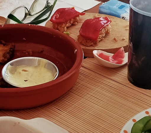 Un plato de madera con sushi de pimiento, el aspecto parece pescado. Al lado se ve un poco de la mayonesa de otro plato 