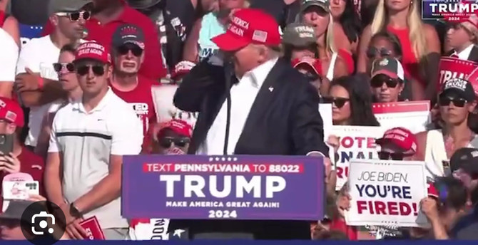 Trump being shot at a fascist rally with people behind him holding placards saying YOU'RE FIRED