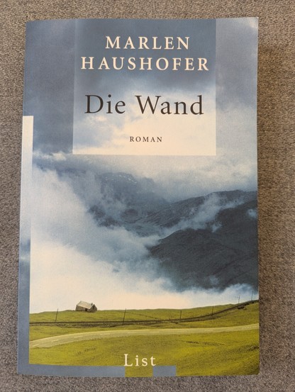 Buchcover, Die Wand von Marlen Haushofer.
Abgebildet, eine Almwiese in den Bergen mit einer Hütte. Wolken stürzen ins Tal.