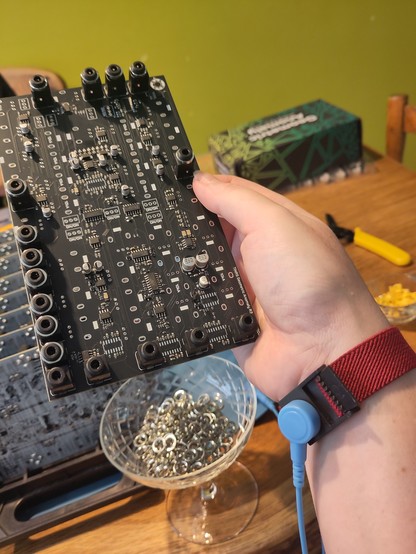 Picture of my hand holding a black PCB with some components already on them and a anti-static wristband on my wrist