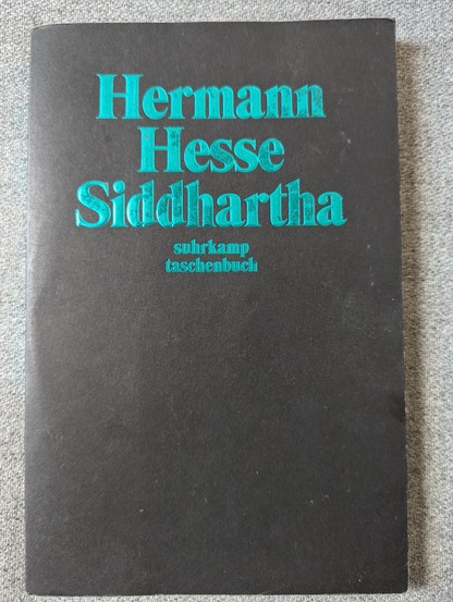 Buchcover, Siddhartha von Hermann Hesse.
Abgebildet, türkisfarbene Schrift auf schwarzem Untergrund.