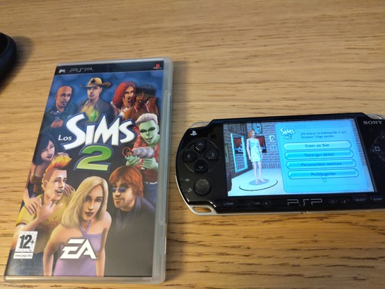 Sims 2 para psp. Se ve la caja el juego y la psp con el juego en marcha