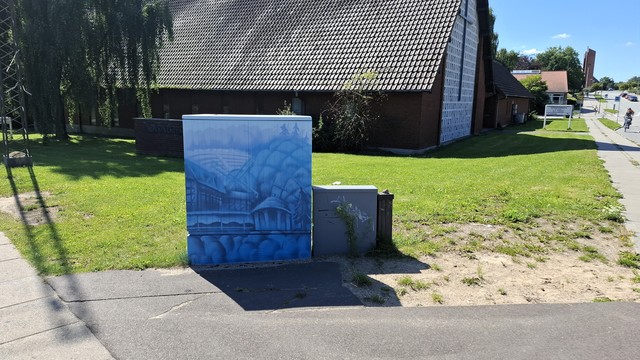 At a crossroads in Aarhus, sun shining, sky blue. Beyond, a glimpse of a modern red-brick church. The gable wall is white with a black cross on it. Beyond, low and tall buildings, a cyclist, parked cars. Left, an electricity pylon is casting its shadow at us. At our feet, a utility box painted a lovely deep sky blue. It depicts scenes from Den Gamle By open-air history museum and the botanical gardens, both of which are close by. We see an old pavilion; an old windmill; the botanic garden’s greenhouse dome; the park’s natural amphitheatre; medieval timbered houses. All sketched like line drawings in blue. A kind of ethereal effect. Now follows same context description for all photos in this thread, if you want to skip. A council utility box for electrical and technical stuff, about half a metre by half a metre in size, normally grey metal box, typically dirty and covered in graffiti and stickers. They have been transformed all across the city in recent weeks, painted on all four sides and on top with images that reflect something in the immediate neighbourhood. Artist signature: J W ’24.