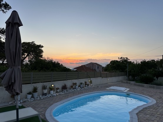 View from a patio over a kidney shaped swimming pool looking to sunset over the Ionian Sea