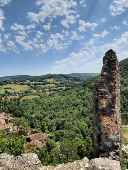 A ruined stone castle wall overlooking a verdant valley below