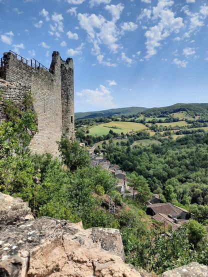 A ruined stone castle wall overlooking a verdant valley below