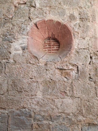 A small round window and a stone wall that has been bricked in