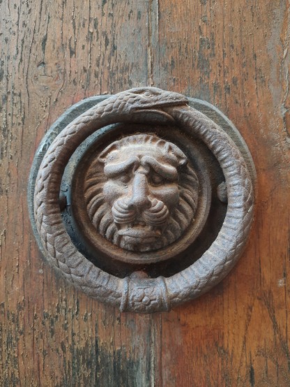 A large old metal doorknocker shaped like a lion head surrounded by an oroboros