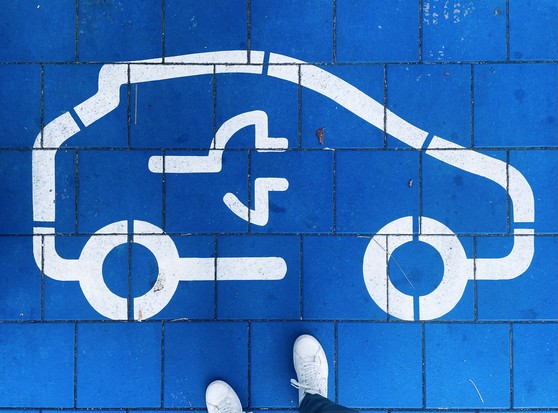 White electric vehicle charging symbol painted on blue tiles, with two white shoes visible at the bottom.