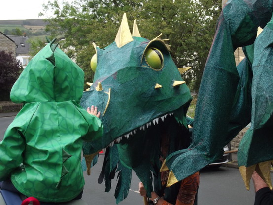 Small child, from behind, wearing dragon costume, 'pets' giant puppet dragon. One of many lovely interactions today.