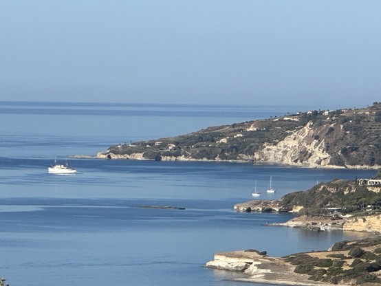 One large white motor yacht and two smaller sailing boats in a cove on a rocky Ionian shoreline 