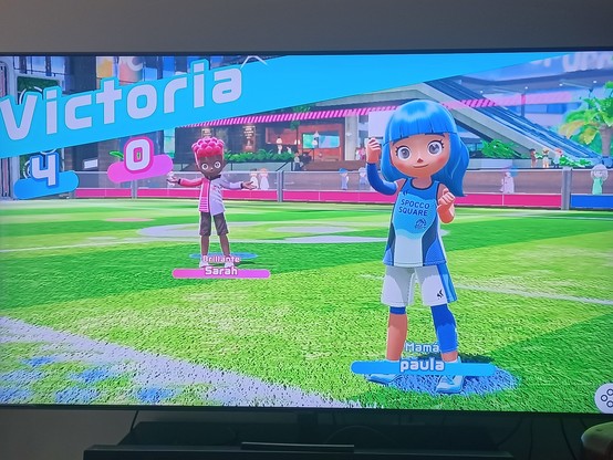 Foto de la pantalla de la tele con dos muñecas del switch sports en un campo de futbol, delante hay una más contenta que la otra en posición de victoria y pone 