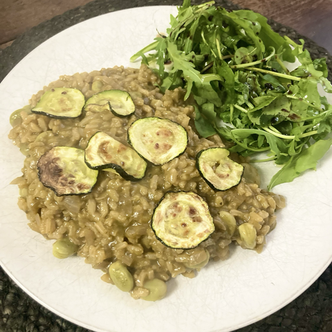 Brown risotto with griddled courgett slices on top on a white plate. Soms rocket watercress and spinach are on the plate, top right