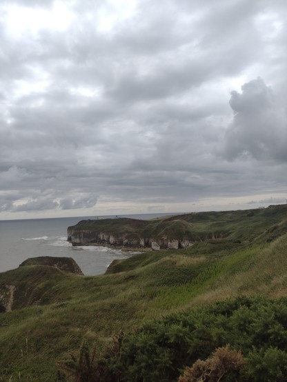 Grassy headland towards the season the left. Cloudy grey sky above.