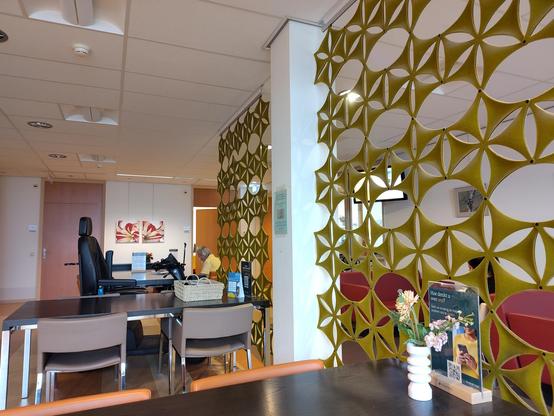 wachtruimte fysiotherapie van het Flevoziekenhuis, tafels, stoelen en half doorzichtige afscheidingen.