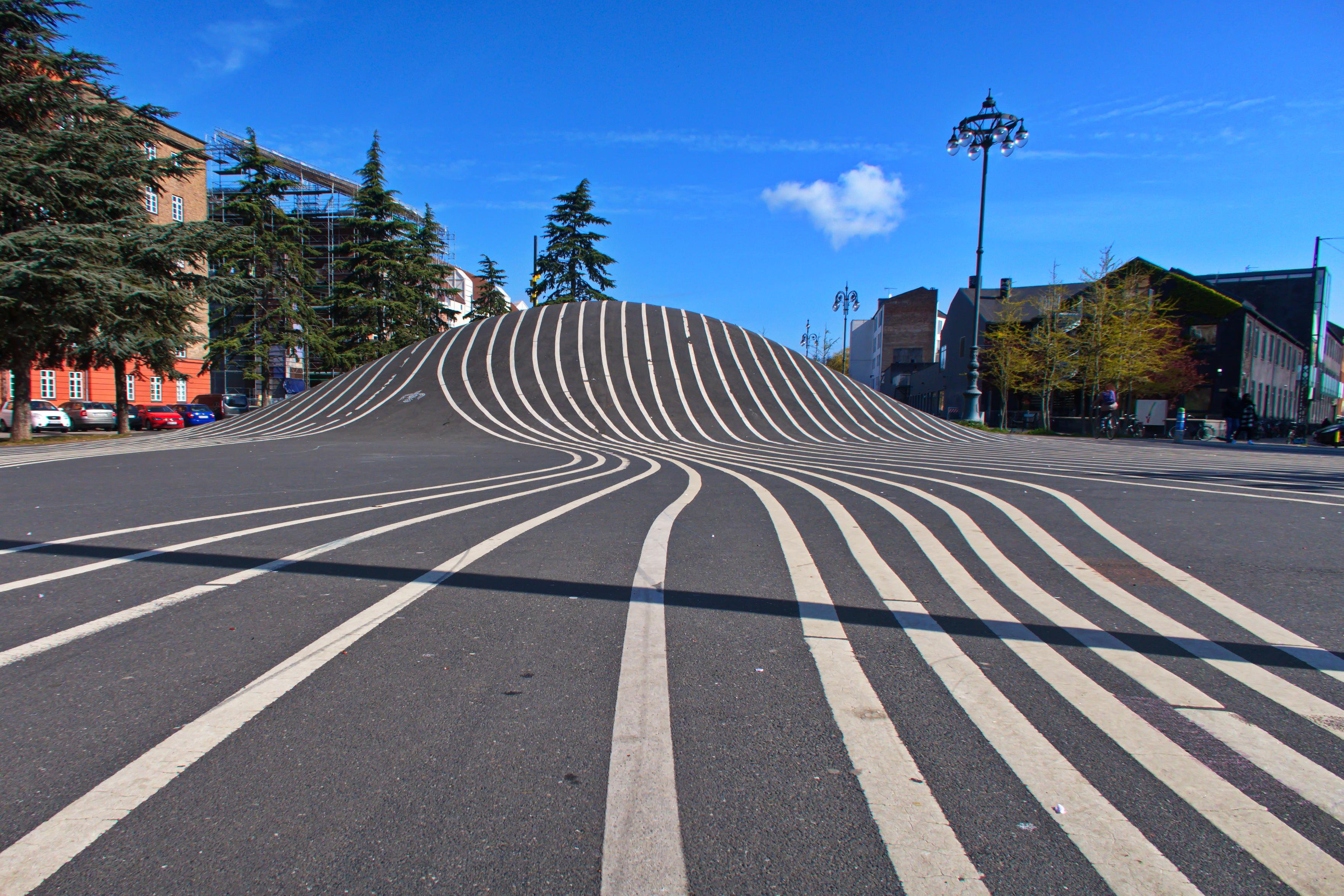 Den Sorte Plads, Superkilen Park, Kopenhagen, Dänemark
Viele Straßenmarkierungen schlängeln sich als Kunstwerk über einen Hügel, ganz rechts davon führt der eigentliche Radweg entlang, auf dem Autofirmen auch schon Werbespots gedreht haben. Den Sorte Plads, Superkilen Park, Kopenhagen, Dänemark
Viele Straßenmarkierungen schlängeln sich als Kunstwerk über einen Hügel, ganz rechts davon führt der eigentliche Radweg entlang, auf dem Autofirmen auch schon Werbespots gedreht haben.