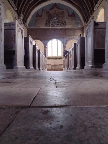 A church window viewed from the perspective of the floor. Wooden Box pews to the left and right .