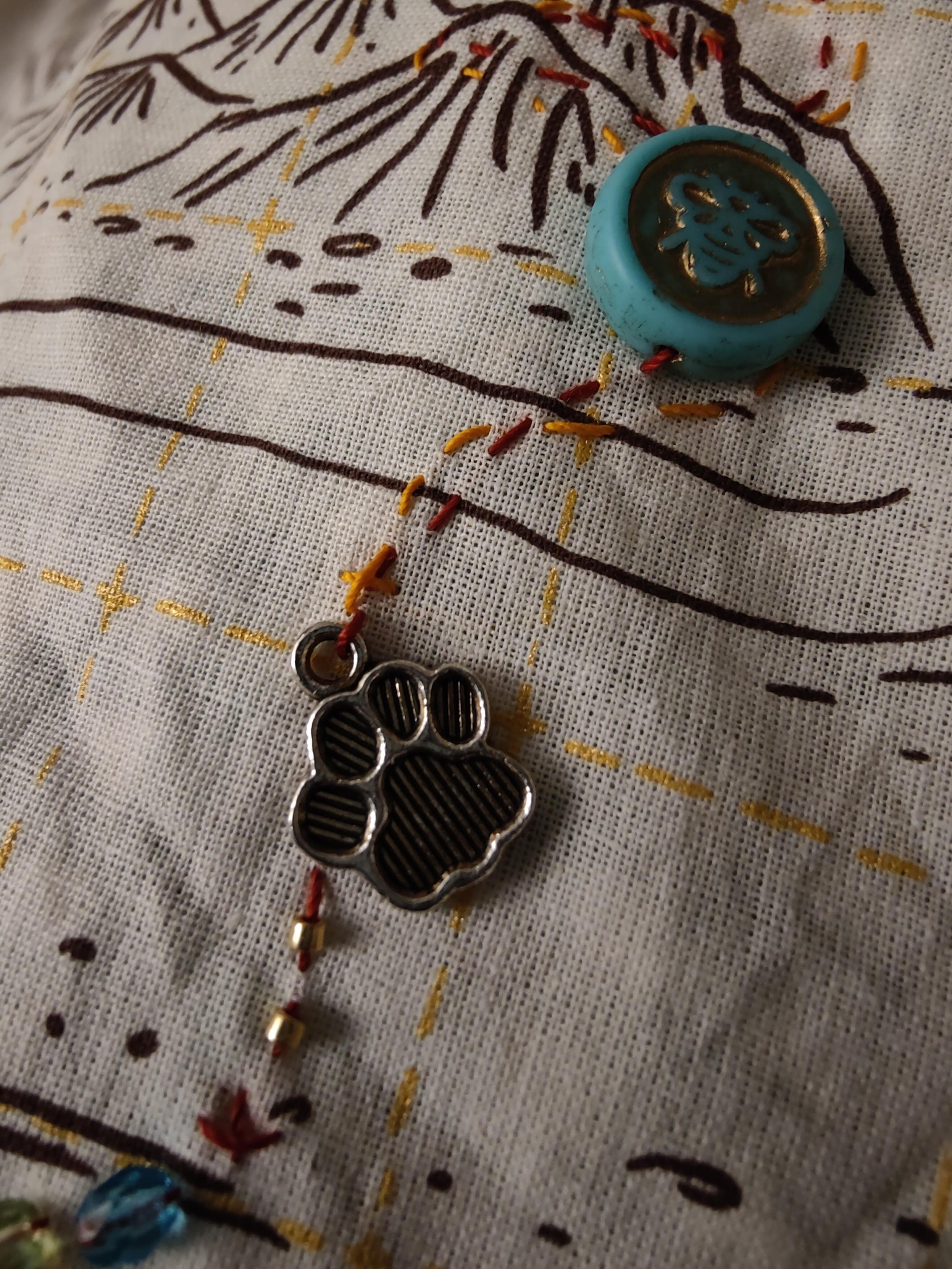Detalle de un bordado con cuentas pequeñas brillantes, un abalori de huella de perro y una cuenta de una abeja