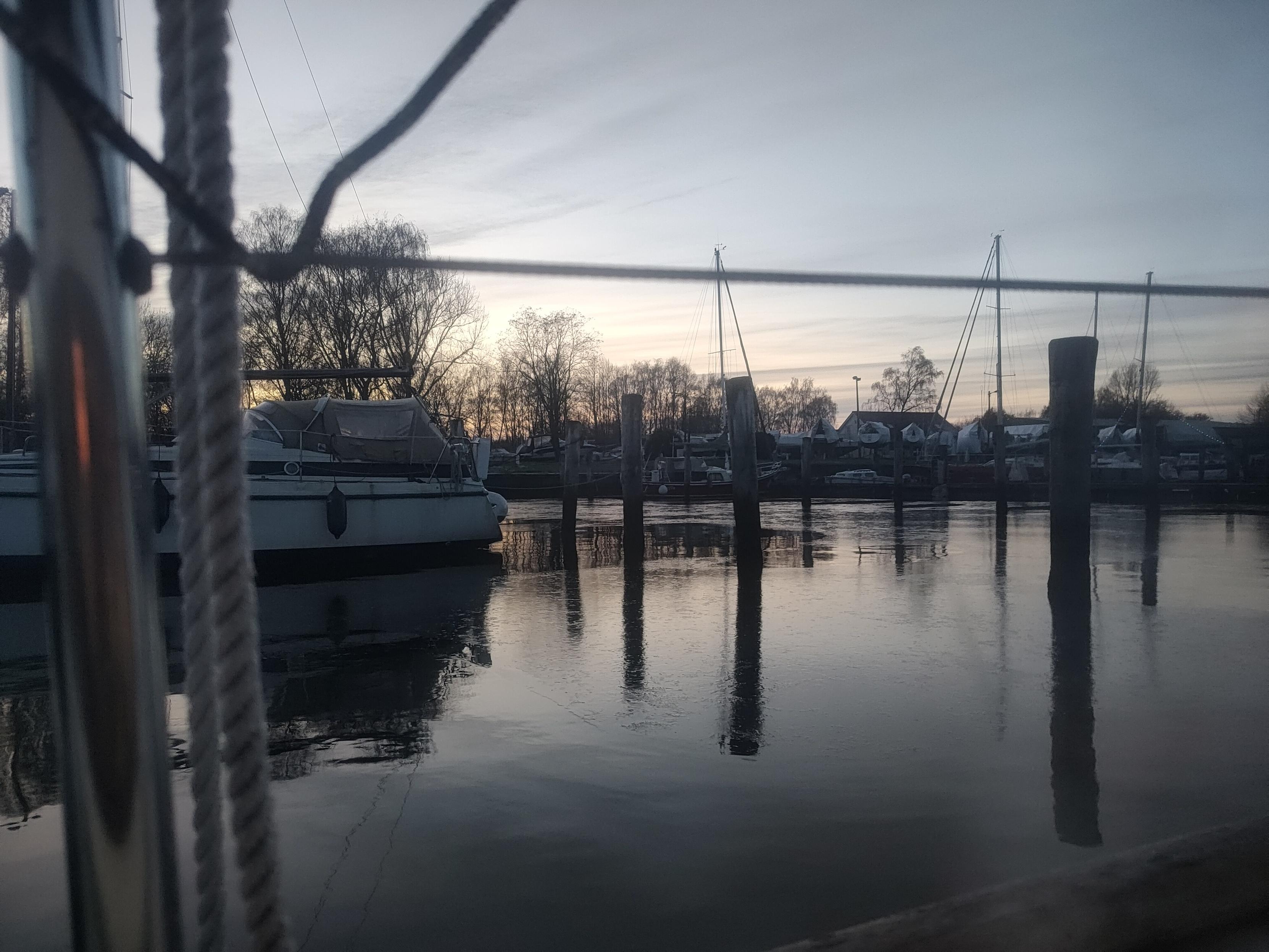 Blick aus dem Fenster eines Segelbootes über das Wasser, teilweise ist eine dünne Eisschicht erkennbar
