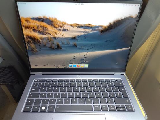 Same notebook on the train table, this time open and working, displaying a Pantheon desktop.