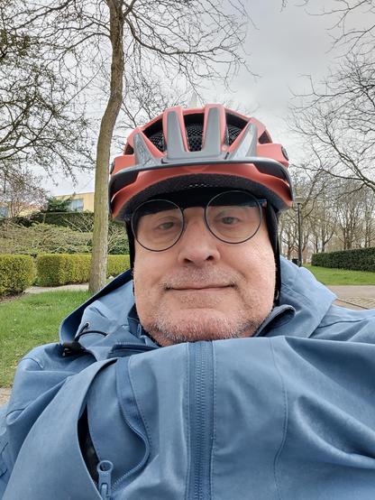 oude man, ongeschoren, rood zwarte fietshelm, zwarte muts, Harry Potter bril, blauw Jack dat heel onelegant opbolt.