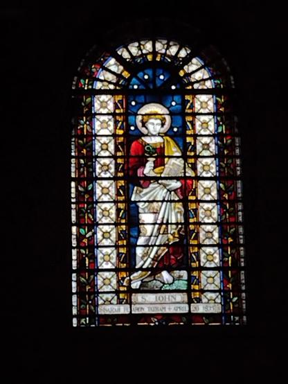 Stained glass window depicting St John on a blue background surrounded by a round topped arch of light glass.