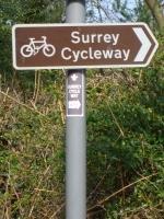 Brown sign on a grey post. Showing a bicycle and in white text "Surrey Cycleway"