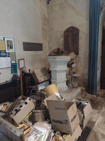 A stone font with a wooden lid surrounded be a diverse collection of detritus 
