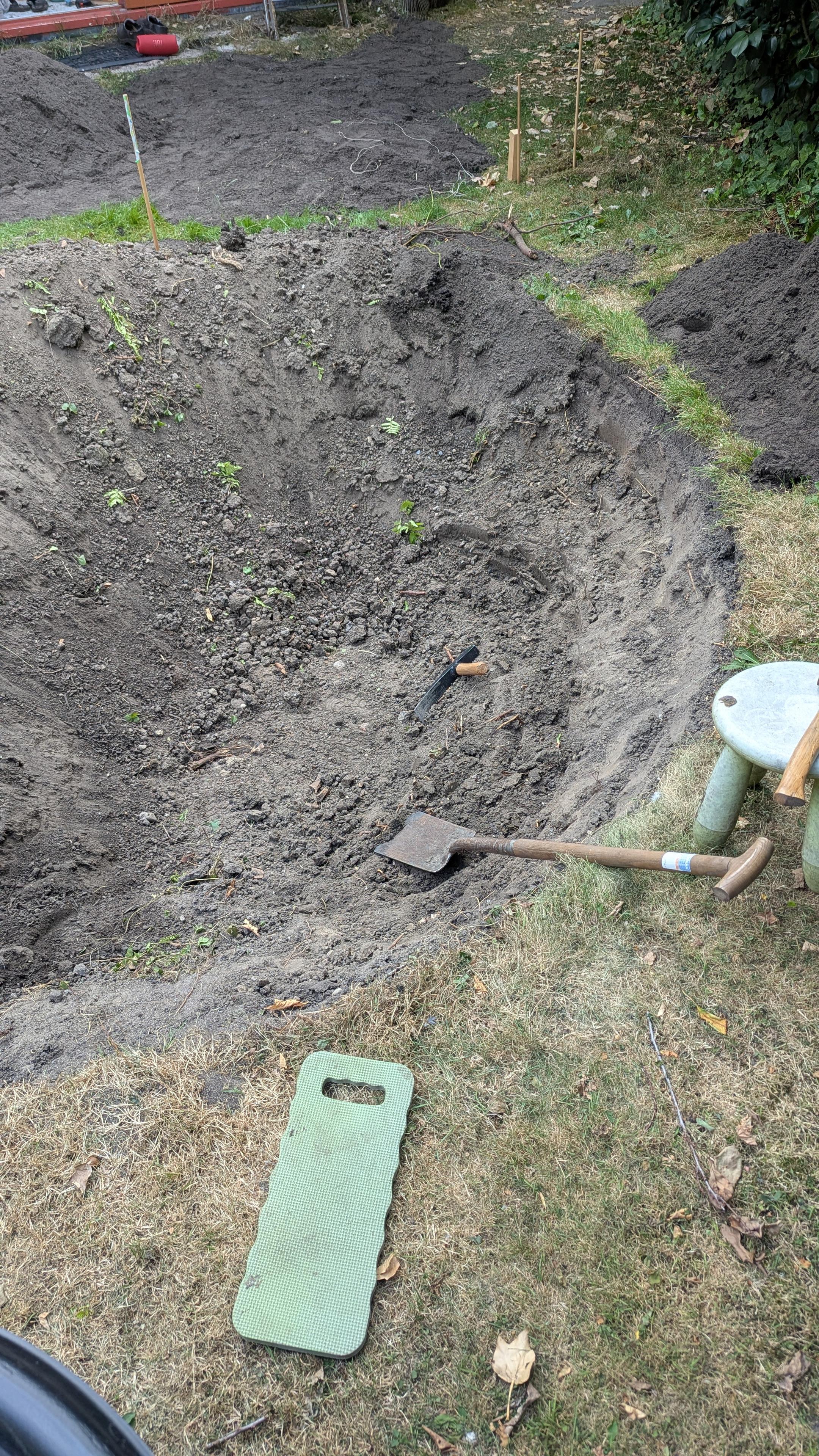 Foto gat in de tuin met paar instrumenten, waaronder een bijl en een spade. En veel droge aarde...