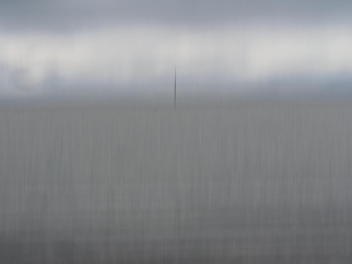 A burred grey scene, with sky at the top and a blurry sea beneath and a ghostly mast in the centre.