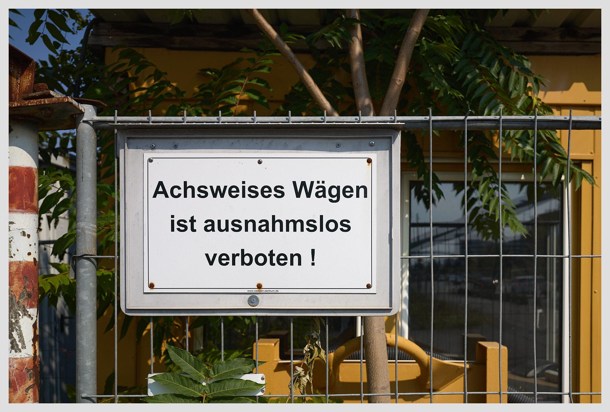 Horizontal image of a sign at the gate of an industrial site. The rough translation is "It is forbidden without any exception to weigh your vehicle axle by axle"