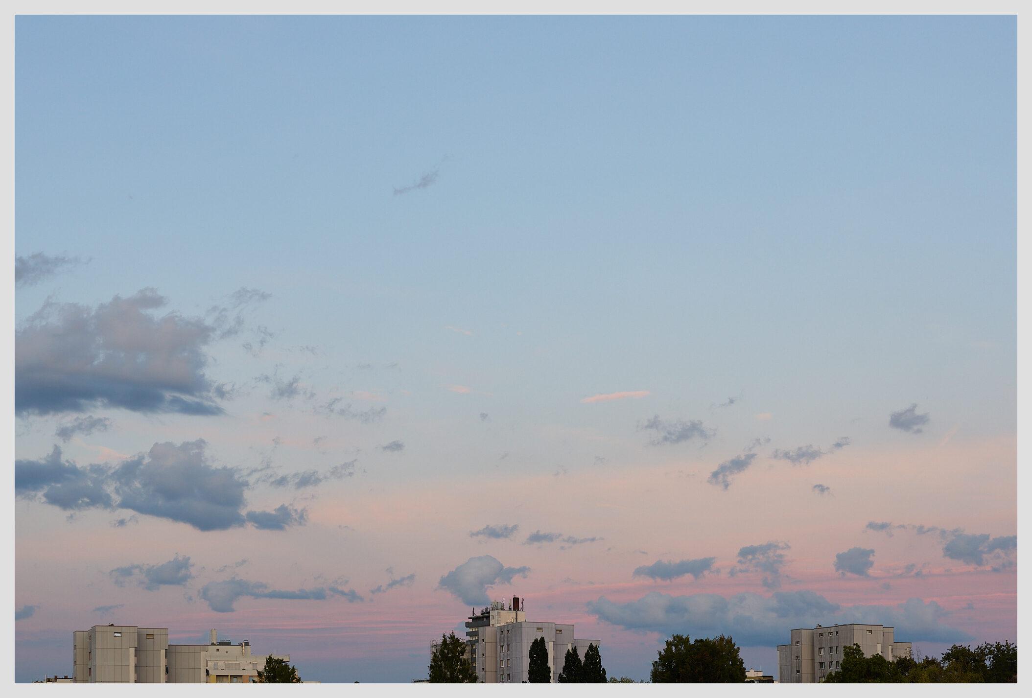 Wide horizontal image of the evening sky with soft, muted colors over some bland apartment towers at the bottom of the frame.
