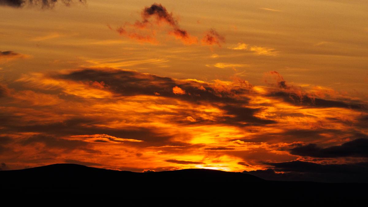 A glorious bright red sunset, with two low rounded hills on a low horizon.