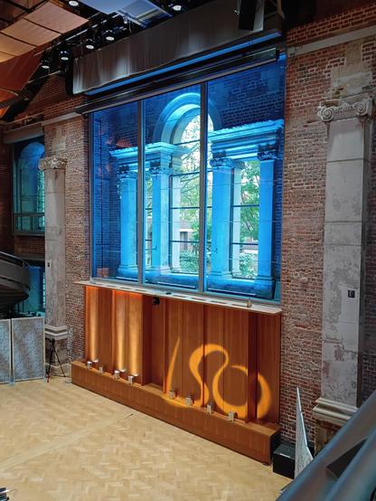 A reworked chancel window with blue lighting and a projected logo LSO beneath, yellow on brown wood panelling.